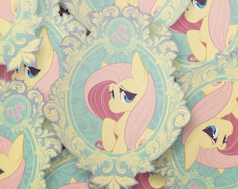 Puede incluir: Una pegatina troquelada que muestra un poni amarillo con una larga crin y cola de color rosa, encerrado en un marco ornamentado de color azul claro con volutas. El diseño incluye tres pequeñas mariposas rosas sobre la cabeza.