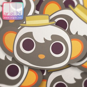 May include: A stack of gray and white animal face stickers with yellow and orange accents. The animal has a white face with black eyes and a brown nose. The animal is wearing a yellow hat.