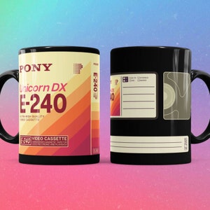 Puede incluir: Taza de café negra con un diseño de cinta de cassette VHS vintage. La cinta está etiquetada "PONY Unicorn DX E-240 Ultra High Quality Video Cassette".