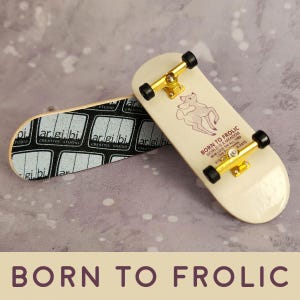 May include: Two miniature skateboards. One has a black and white graphic with the text "ar.gi.bi CREATIVE STUDIO". The other has a white background with a pink deer graphic and the text "BORN TO FROLIC WORLD IS A MEADOW LOVE EM ALL 1989 WWW.LOVEEMALL.COM BLEATS".