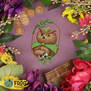 May include: Cross stitch pattern featuring a brown owl wearing a green hat and cloak, perched on a branch with green leaves. The owl is surrounded by gold coins and purple flowers.