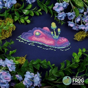May include: Cross stitch pattern of a purple, pink, and blue butterfly with a yellow mushroom growing on its back. The butterfly is surrounded by green leaves and blue flowers. The pattern is on a dark blue fabric. The text "FINE FROG STITCHING" is in the bottom right corner of the image.