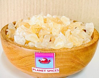 Puede incluir: Un bol de madera lleno de trozos translúcidos, de color marrón claro e irregulares de fruta seca. El bol tiene una etiqueta que dice "Planet Spices".