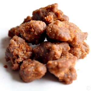 Puede incluir: Un mont&oacute;n de caramelos marrones de forma irregular con una superficie texturizada y ligeramente granulada. Los caramelos presentan una mezcla de tonos marrones oscuros y claros, lo que sugiere un recubrimiento caramelizado o azucarado. La imagen est&aacute; sobre un fondo blanco liso.