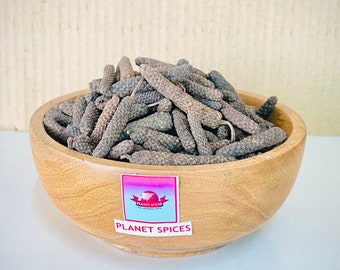 Puede incluir: Un bol de madera lleno de granos de pimienta larga secos. El bol tiene una etiqueta que dice "Planet Spices".