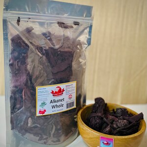 May include: A clear plastic resealable pouch containing dried Alkanet root pieces with a white label reading Planet Spices Alkanet Whole Net Wt. 100 g (3.53 oz). Next to it is a small round wooden bowl filled with the same dark purple-brown root pieces.