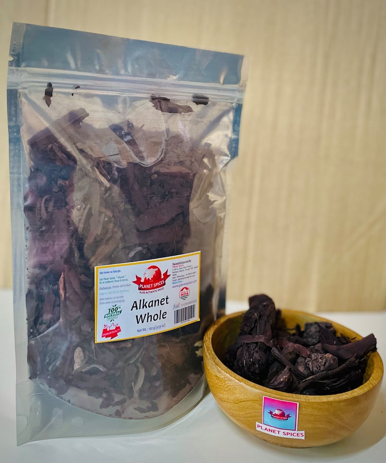 May include: A clear plastic resealable pouch containing dried Alkanet root pieces with a white label reading Planet Spices Alkanet Whole Net Wt. 100 g (3.53 oz). Next to it is a small round wooden bowl filled with the same dark purple-brown root pieces.