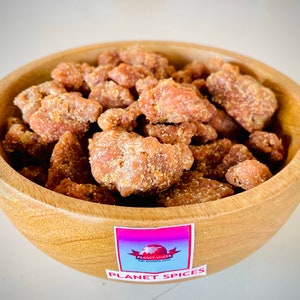 May include: A wooden bowl filled with brown, irregularly shaped pieces of  jaggery, a type of unrefined cane sugar. The bowl has a sticker on the bottom that says "Planet Spices".