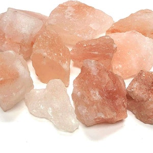 May include: A collection of raw, unrefined Himalayan salt chunks in varying shades of pale pink, translucent white, and soft orange. These jagged, crystalline mineral rocks feature irregular, angular shapes and a natural, rough-textured surface.