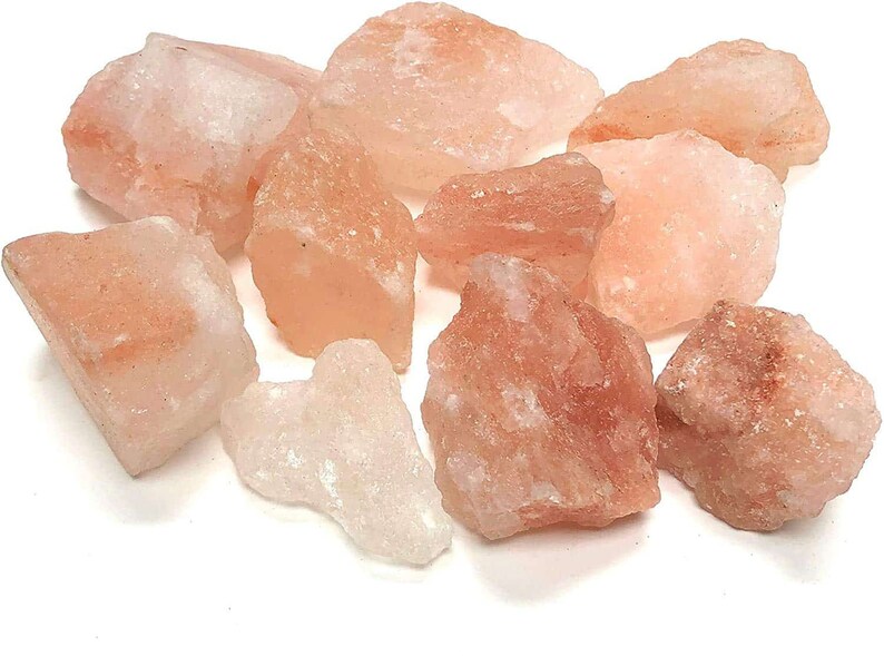May include: A collection of raw, unrefined Himalayan salt chunks in varying shades of pale pink, translucent white, and soft orange. These jagged, crystalline mineral rocks feature irregular, angular shapes and a natural, rough-textured surface.