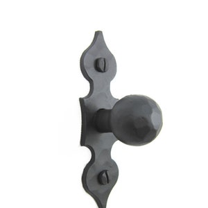 May include: Black metal door knob with a rounded handle and a decorative backplate with a pointed design.