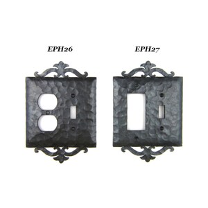 May include: Two black metal light switch and outlet covers with an ornate design. The cover on the left is labeled EPH26 and has a double outlet and a single switch. The cover on the right is labeled EPH27 and has a single switch and a single outlet.