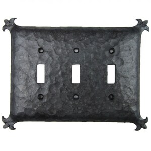 May include: A black metal light switch plate with a hammered finish and decorative fleur-de-lis accents. The plate has three switch openings.