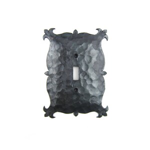 May include: Black metal light switch cover with an ornate design. The cover has a hammered finish and a single switch opening.