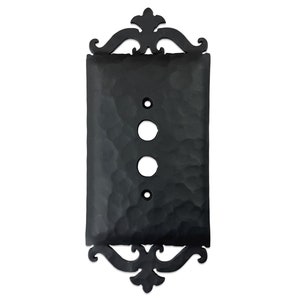 May include: Black metal switch plate with an ornate design and a hammered finish. The plate has three holes for electrical outlets.