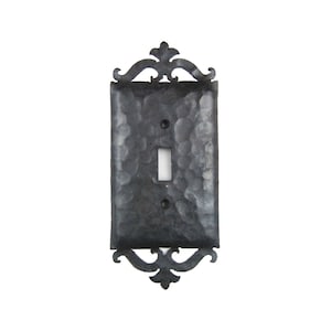 May include: A black metal light switch cover with an ornate design. The cover has a hammered finish and a single switch opening.