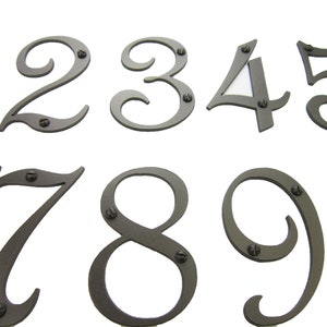May include: Set of ten metal house numbers in a cursive font. The numbers are painted a dark gray color and have a distressed finish. Each number has two small screws for mounting.