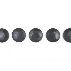 May include: Five black metal coasters with a hammered finish. The coasters are round and have a slightly raised edge.