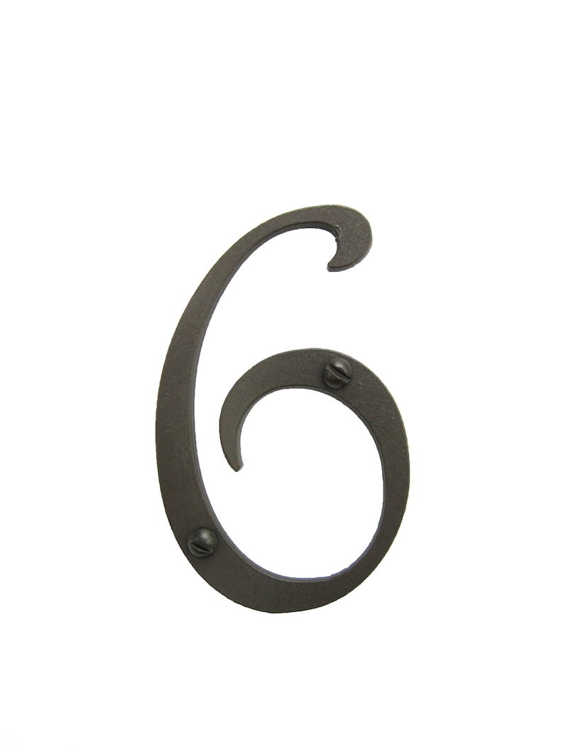 May include: A black metal house number six with a decorative, stylized font. The number is attached to a surface with two visible screws.