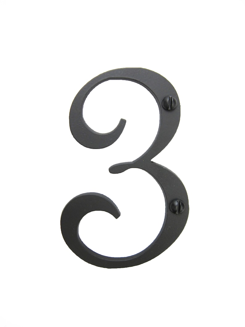 May include: Black metal house number three with a decorative, stylized font. The number is attached to a surface with two screws.