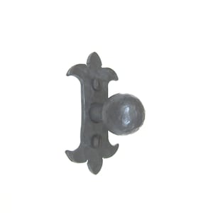 May include: A black metal door knob with a round, textured handle and a decorative, fleur-de-lis shaped backplate.