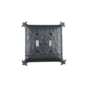 May include: A black metal double toggle light switch cover with a hammered finish and decorative fleur-de-lis accents.