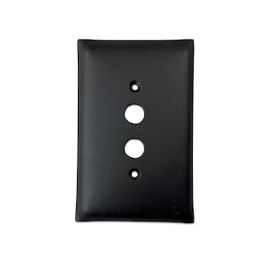 May include: Black metal wall plate with three round holes. The plate has a slightly rounded edge.