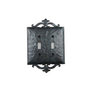 May include: A black metal double light switch cover with an ornate design. The cover has a hammered finish and is designed to fit a standard double switch.
