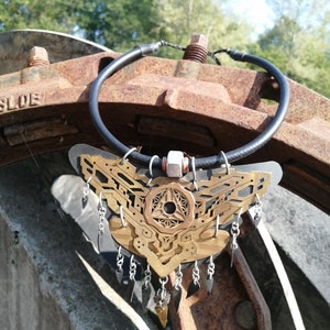 Puede incluir: Un collar de oro y plata con un diseño geométrico y colgantes. El collar está hecho de metal y tiene un cordón de cuero negro.