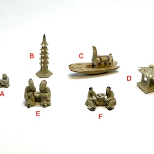 May include: A collection of six miniature beige ceramic figurines labeled A through F. The set includes two pairs of seated figures, a tall multi-tiered pagoda, a small boat with a cabin, and a square pavilion structure with a peaked roof.