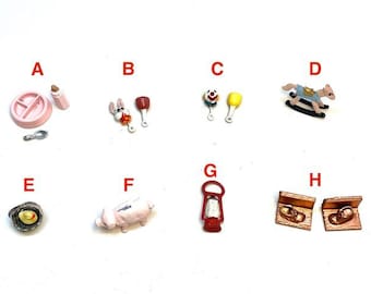 Op de afbeelding: Een verzameling miniatuur speelgoedbedels gelabeld van A tot H. De items bevatten een roze bord en fles, een konijn, een rammelaar, een hobbelpaard, een eend in een nest, een varken, een rode lantaarn en twee stoelen in houtstijl.