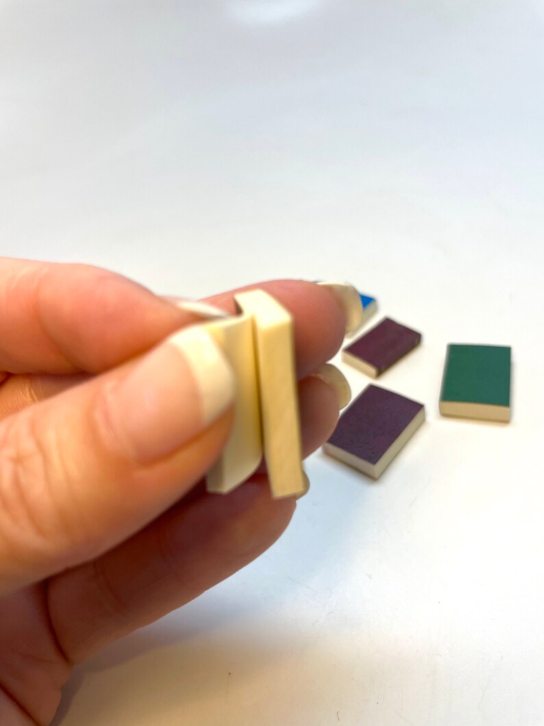 Op de afbeelding: Een hand die twee kleine, witte, rechthoekige blokken vasthoudt. Er liggen drie andere kleine, rechthoekige blokken op de tafel, een blauwe, een groene en een paarse.
