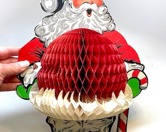 May include: A vintage paper Santa Claus cutout with a red and white honeycomb ball. Santa is wearing a red suit, white beard, and black boots. He is holding a candy cane.