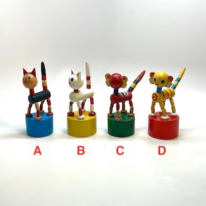 May include: Four colorful wooden animal toys. Each toy has a round base and a body made of wooden beads. The animals include a cat, a monkey, and a tiger. The bases are painted blue, yellow, green, and red. The toys are labeled A, B, C, and D.