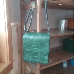 May include: A green leather crossbody bag with a crocodile embossed pattern. The bag has a long adjustable strap and a flap closure.