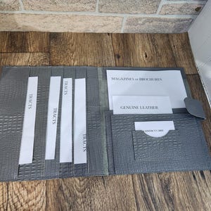 May include: Gray leather folder with pockets for magazines, brochures, tracts, and a business card. The folder has a crocodile embossed pattern.
