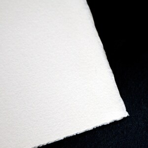 Puede incluir: Primer plano de una hoja de papel blanca texturizada con una superficie ligeramente rugosa. El papel est&aacute; colocado sobre un fondo negro.
