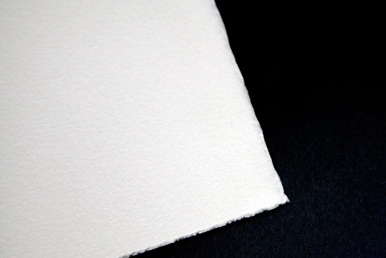 Puede incluir: Primer plano de una hoja de papel blanca texturizada con una superficie ligeramente rugosa. El papel est&aacute; colocado sobre un fondo negro.
