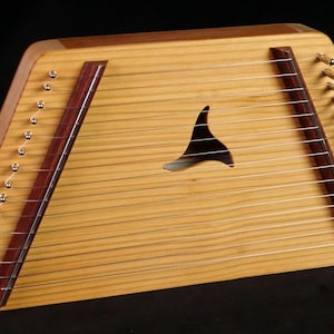 Könnte beinhalten: Eine Holzharmonie mit natürlicher Oberfläche. Das Instrument hat ein Schallloch in Form einer stilisierten Flosse, Saiten und Stimmwirbel. Dunkelbraune Akzente umrahmen die Saiten.