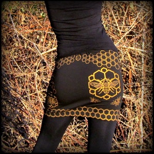 Peut inclure: Une jupe noire avec un motif en nid d'abeille doré et un motif d'abeille. La jupe est faite d'un tissu doux et extensible et a une coupe confortable.