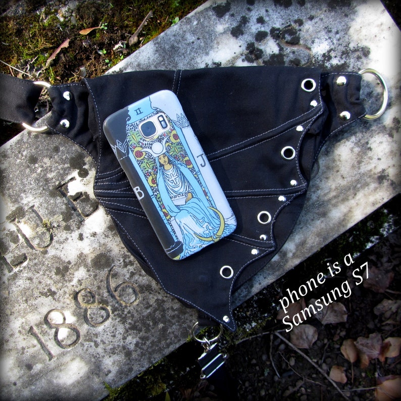 May include: A black fabric belt with silver grommets and a phone case featuring the High Priestess card from a tarot deck. The phone is a Samsung S7.