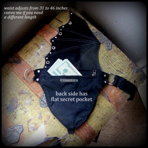 May include: Black fabric waist belt with a zippered pocket and a hidden pocket on the back. The belt is adjustable from 31 to 46 inches. "Talismana Designs" is printed on the front pocket.