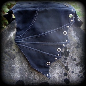 May include: Black canvas bag with a wing-shaped flap. The flap has white stitching and silver grommets and studs.