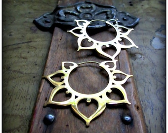 May include: A pair of gold-toned hoop earrings with a delicate, intricate design. The earrings are shaped like a flower with a circular center and multiple petals.