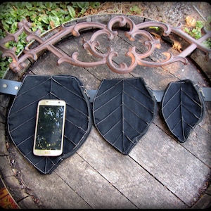 May include: A black leather belt with three leaf-shaped pouches. The pouches have zippers and are lined with black fabric. A gold smartphone is in the left pouch.