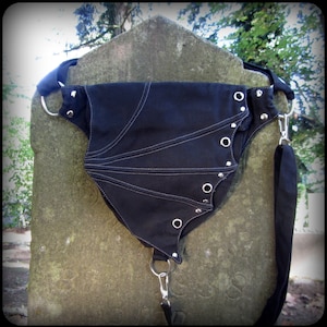 May include: Black canvas fanny pack with silver grommets and a white stitching detail. The bag has a long adjustable strap.