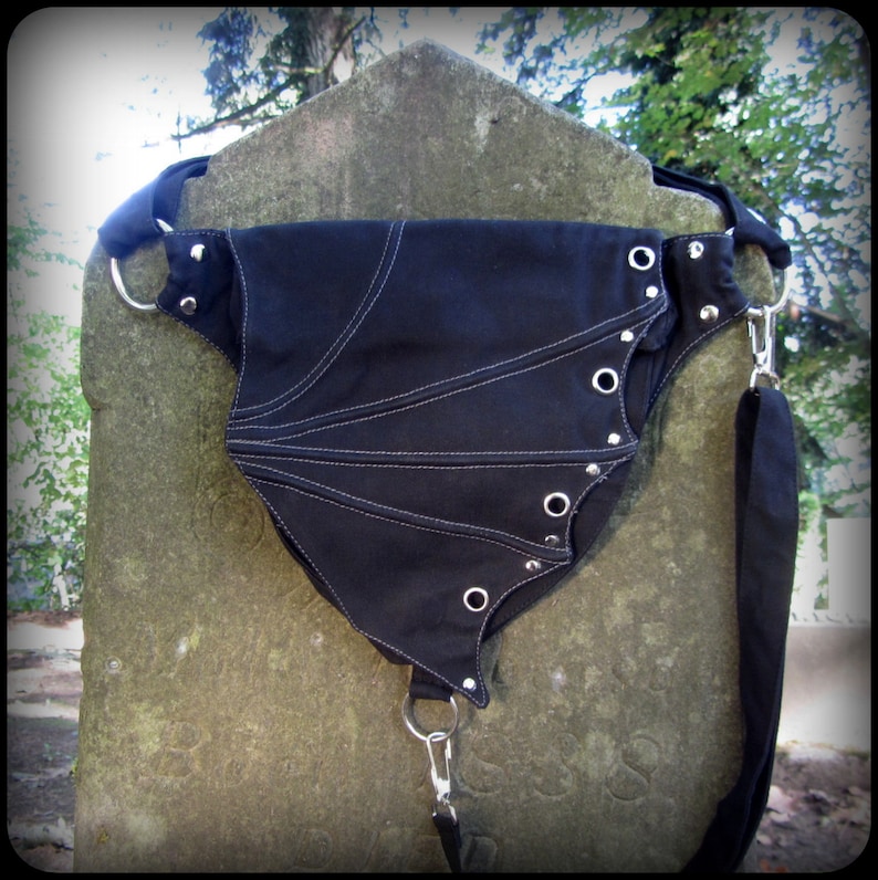 May include: Black canvas fanny pack with silver grommets and a white stitching detail. The bag has a long adjustable strap.