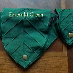 Op de afbeelding: Smaragdgroene stoffen tas in bladvorm met een ritssluiting en een gouden knoop. De tas is onderdeel van een set van drie tassen.