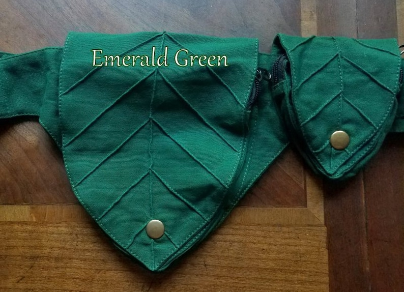 Op de afbeelding: Smaragdgroene stoffen tas in bladvorm met een ritssluiting en een gouden knoop. De tas is onderdeel van een set van drie tassen.