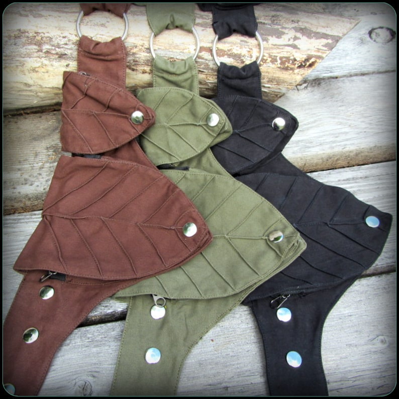Op de afbeelding: Drie stoffen riemen met bladeren-vormige zakken en zilveren drukknopen. De riemen zijn bruin, groen en zwart.